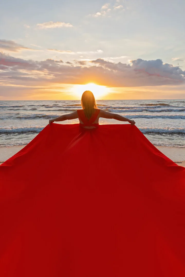 Czerwona suknia Flying Dress rozłożona na plaży na tle zachodu słońca