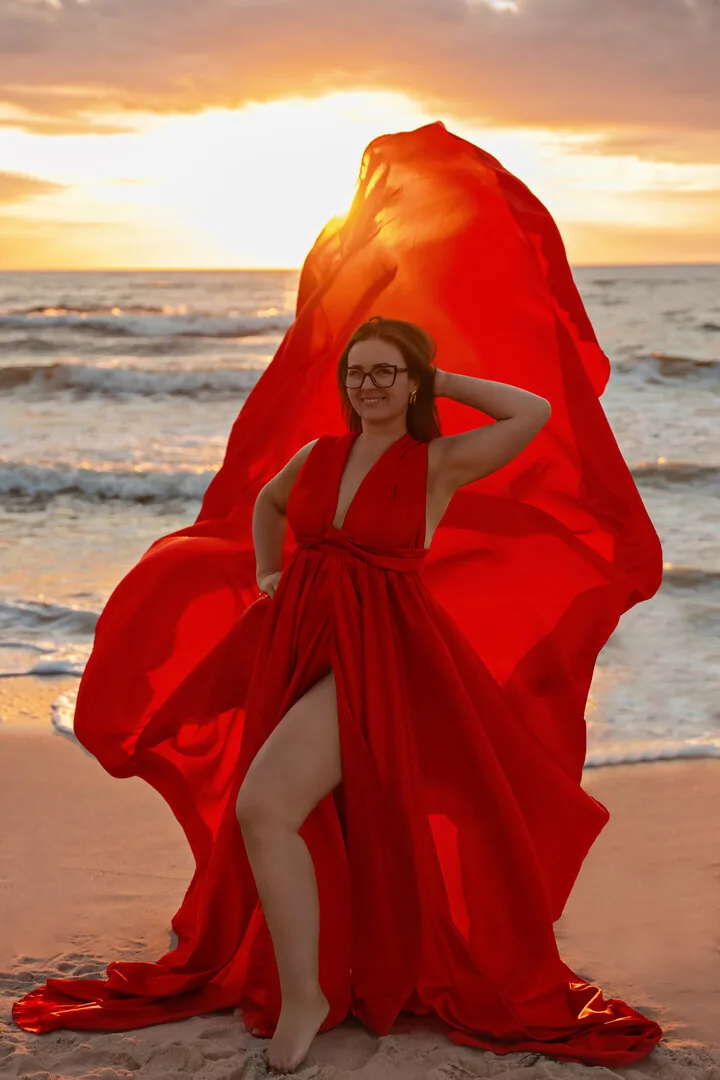Kobieta w czerwonej sukni Flying Dress z trenem uniesionym nad głową
