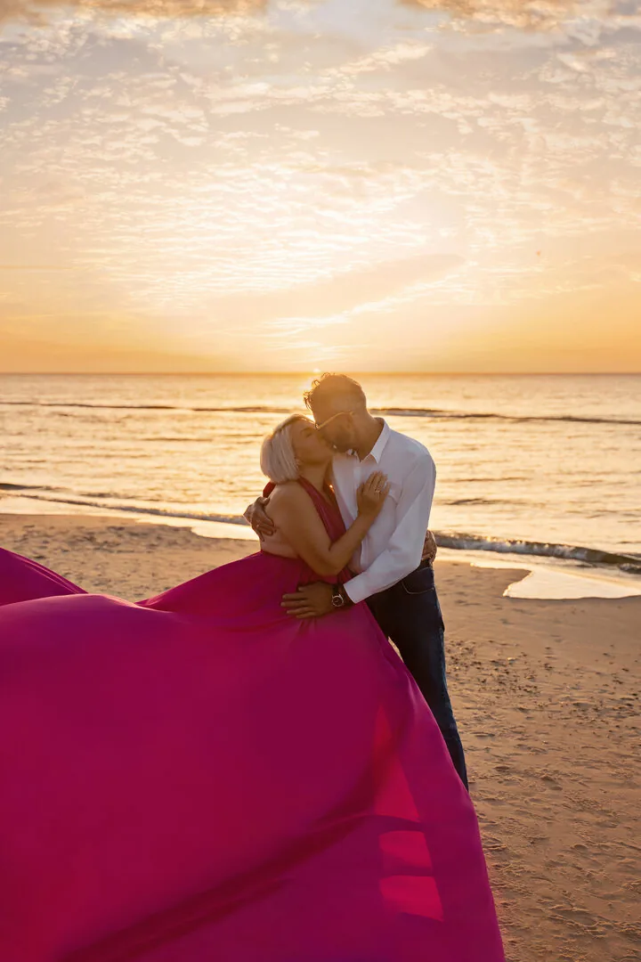 Couple kissing on the beach during a fuchsia Flying Dress photoshoot