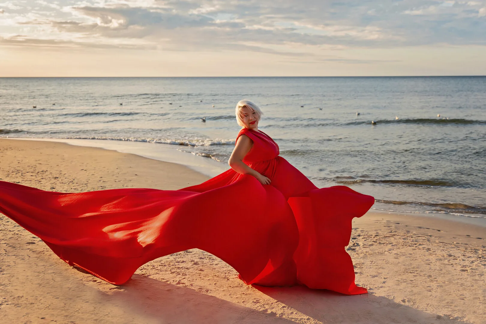 Woman in a red Flying Dress with a flowing train on the beach