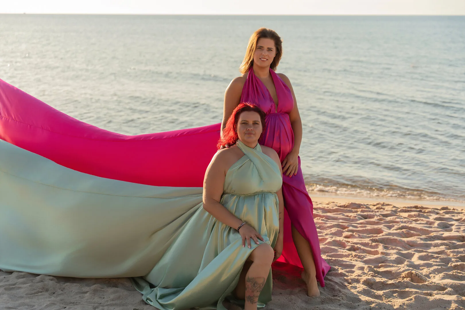 Two women in fuchsia and sage Flying Dresses on the sand
