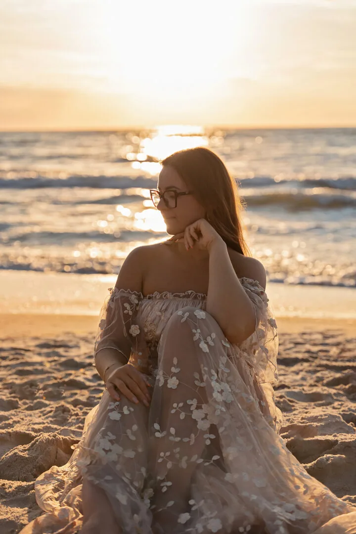 Kobieta w długiej sukni na plaży o zachodzie słońca