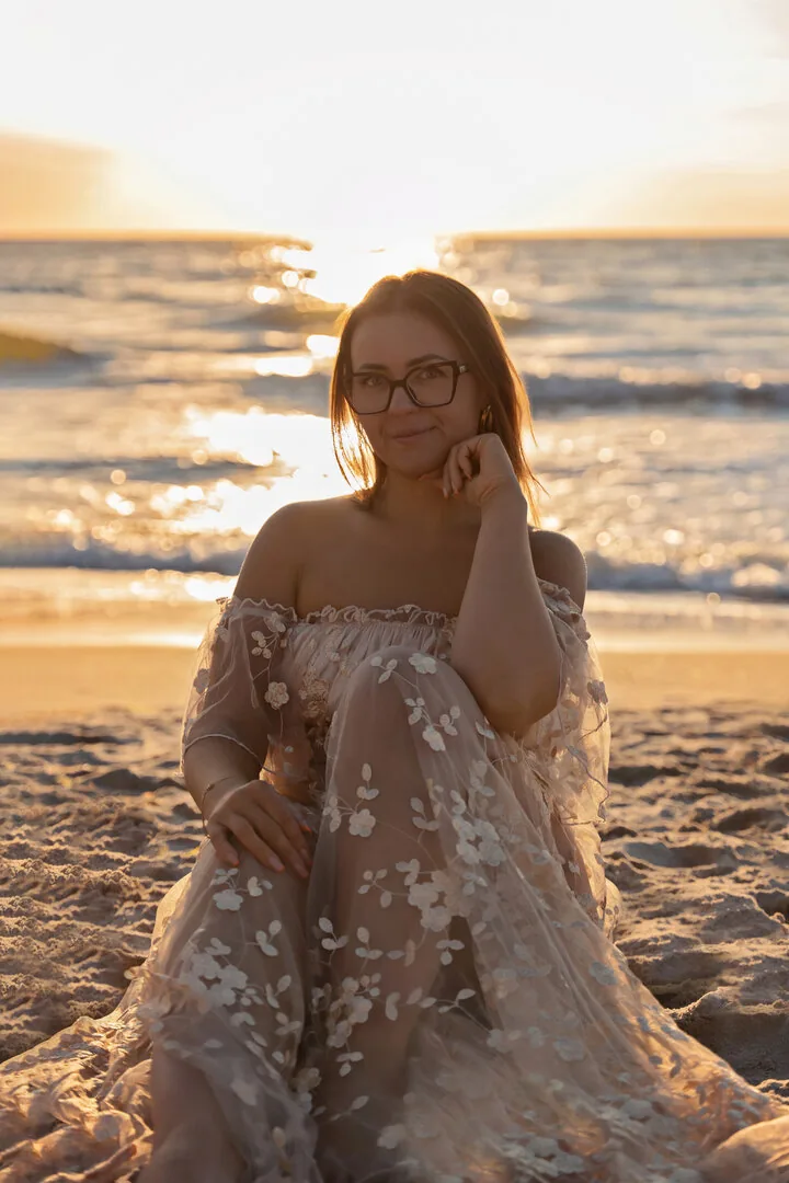 Kobieta w długiej sukni na plaży o zachodzie słońca