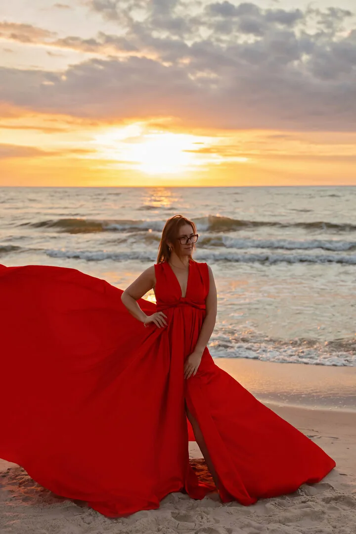 Kobieta w długiej sukni na plaży o zachodzie słońca